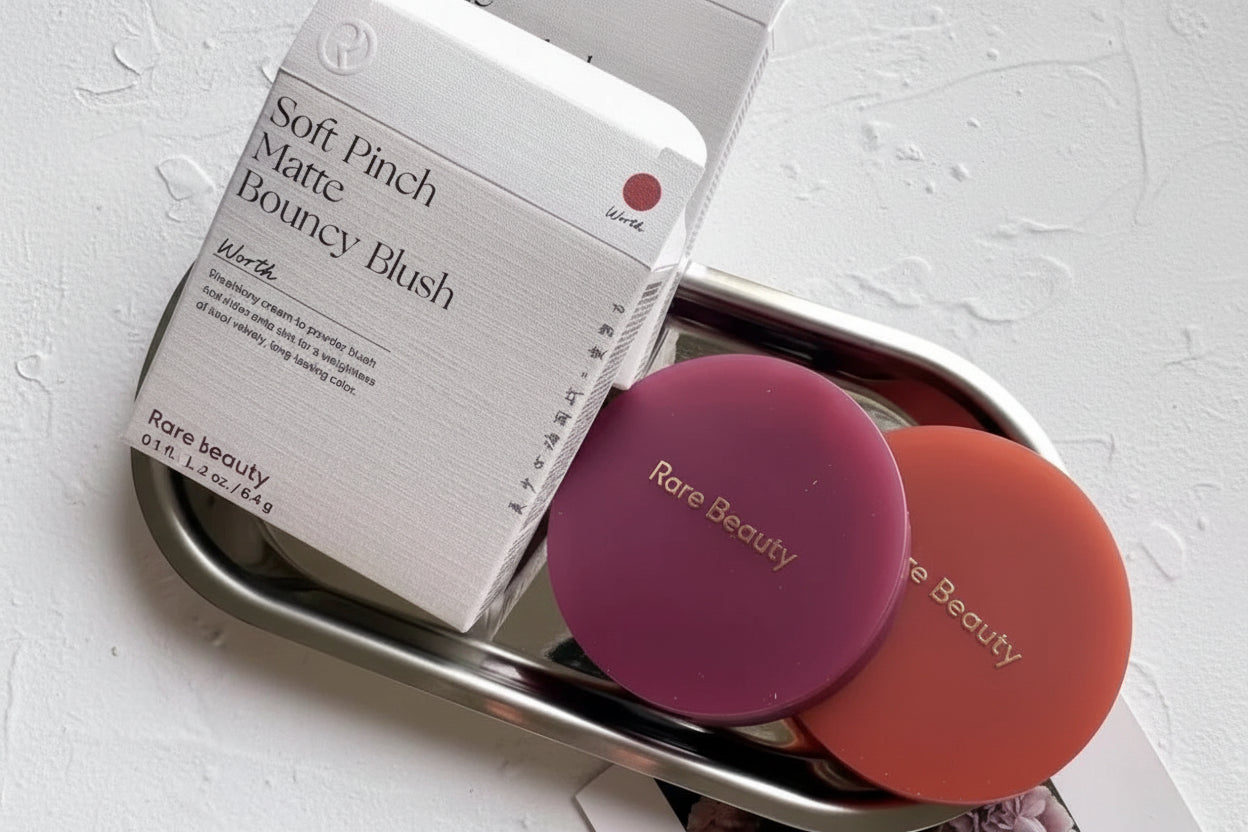 Two blushes with 'Rare Beauty' branding on a metal tray next to their packaging.