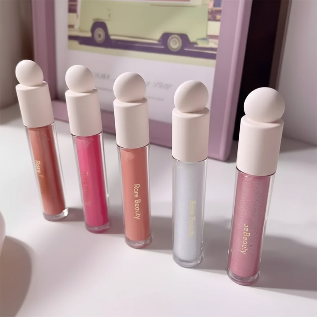 Set of lip glosses with white caps on a light surface, with a blurred background.